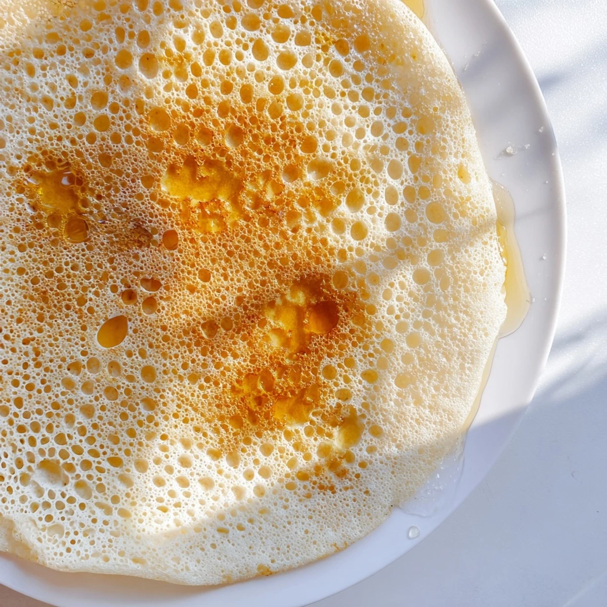 Fluffy Moroccan Baghrir pancakes, bubbly and golden, are ready to be drizzled with sweet, warm honey.