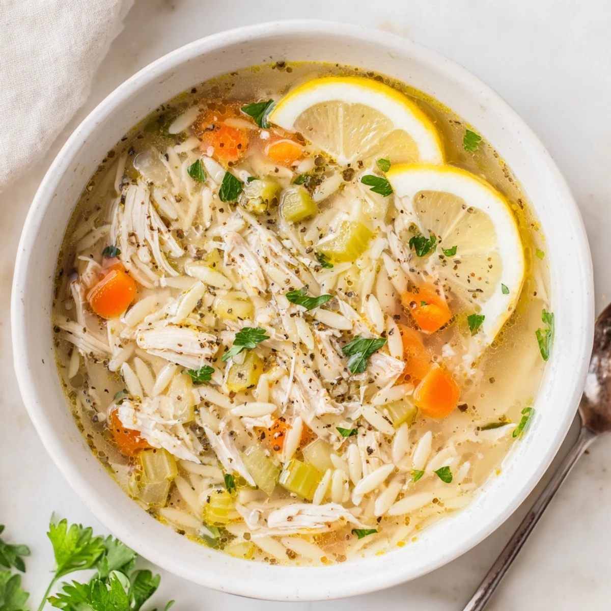 A steaming bowl of Lemon Pepper Chicken Orzo Soup garnished with fresh parsley and lemon wedges, ready to serve.  