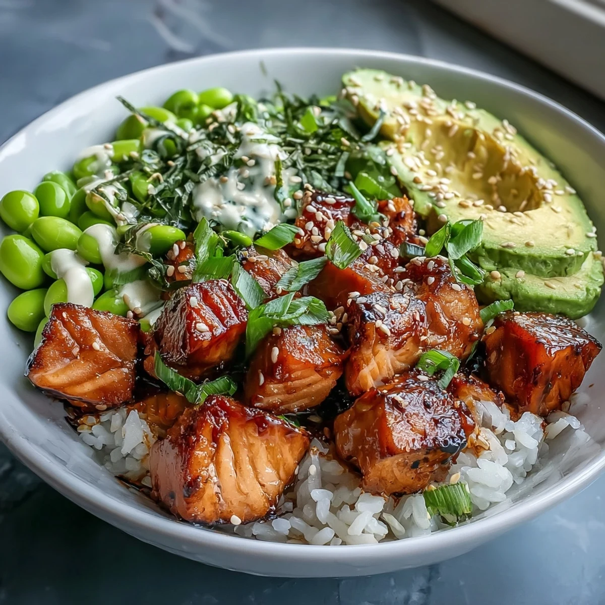 Close-up of a vibrant Salmon Rice Bowl showing marinated salmon, avocado, edamame, and rice on a white plate.