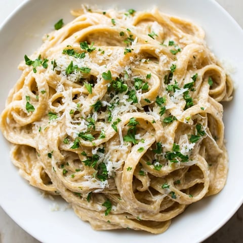 Steaming plate of Skinny Alfredo Garlic Parmesan Snowy Pasta with fresh parsley and extra Parmesan.