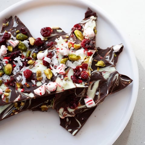 Festive Holiday Bark shards displaying colorful toppings of peppermint, pistachios, and cranberries, ideal for gifting.
