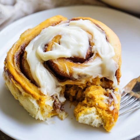 Fluffy cinnamon rolls with pumpkin purée, topped with rich frosting for cozy mornings.  