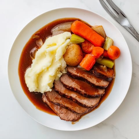 A close-up shot of juicy pot roast with gravy, spooned over fluffy mashed potatoes.