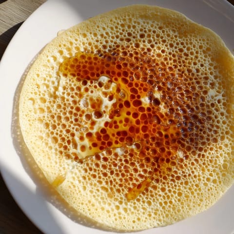 A stack of airy Moroccan Baghrir, with its signature holes, is served with melted butter and honey.