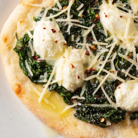 Crispy thin-crust spinach ricotta pizza topped with creamy dollops, garlic butter, and Parmesan served beside a glass of white wine.