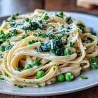 Creamy lemon pasta with peas and spinach, garnished with Parmesan and fresh chives.